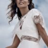 Femme portant une robe de mariée en dentelle raffinée avec des détails délicats, capturée sous un ciel nuageux