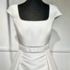 Une robe de mariée princesse à col carré et jupe volumineuse, devant un paysage moderne baigné de lumière.