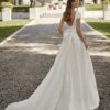 Vue arrière d’une robe de mariée avec un dos échancré, un grand nœud en satin et une longue traîne élégante, posant devant un château.