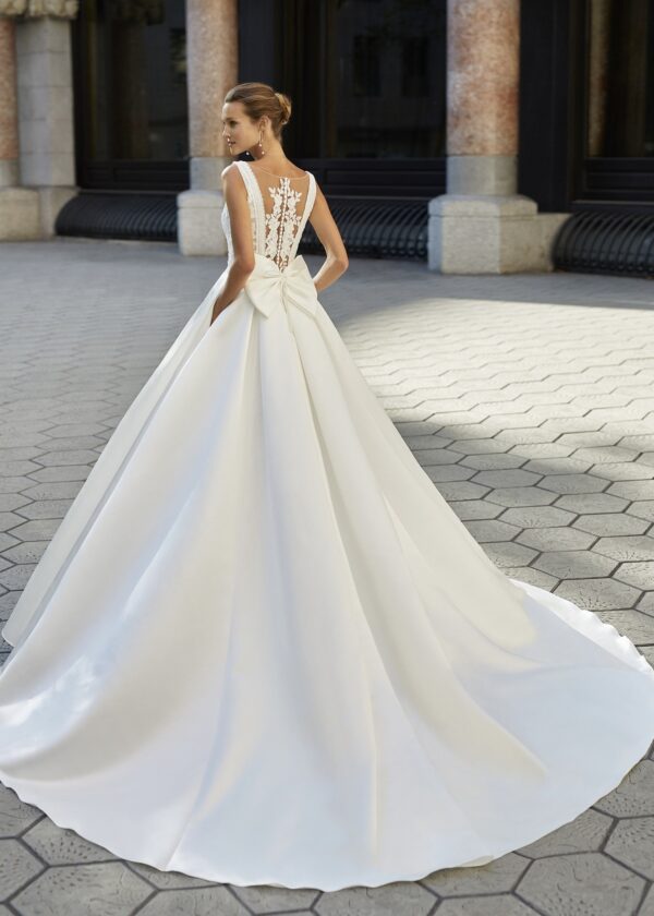 Vue arrière d'une robe de mariée blanche avec un dos en dentelle transparente orné de motifs floraux, une grande jupe volumineuse et un nœud élégant à la taille.