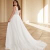 Vue arrière d'une mariée élégante portant une robe à dos en dentelle avec une jupe fluide qui s'étend en une légère traîne, posant dans un cadre architectural lumineux avec des colonnes