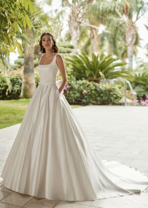 Mariée élégante portant une robe de mariée Mikado satinée avec un col carré et une jupe volumineuse, posant dans un cadre tropical