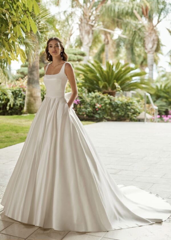 Mariée élégante portant une robe de mariée Mikado satinée avec un col carré et une jupe volumineuse, posant dans un cadre tropical