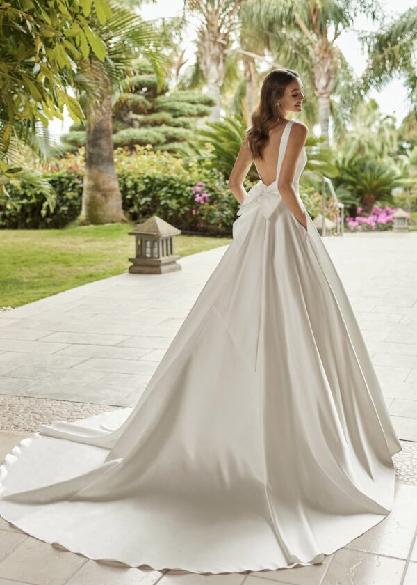 Vue de dos d'une mariée portant une robe de mariée Mikado satinée avec un grand nœud élégant et une traîne majestueuse, dans un cadre tropical