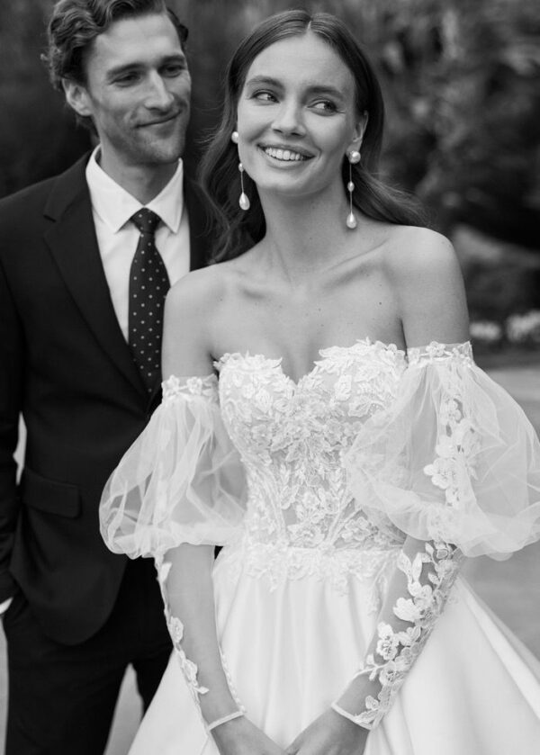 Couple de jeunes mariés souriant, la mariée en robe à manches bouffantes en dentelle, photographie en noir et blanc