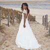 Mariée souriante en robe blanche avec un dos ouvert élégant, marchant sur un chemin de sable avec une vue sur la plage et l'océan en arrière-plan