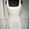 Cette robe de mariée allie minimalisme et élégance avec son corsage ajusté à col carré et sa jupe fluide prolongée d’une traîne légère. Son design épuré s’harmonise parfaitement avec un cadre méditerranéen raffiné, idéal pour une mariée au style intemporel.