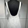 Cette robe de mariée allie minimalisme et élégance avec son corsage ajusté à col carré et sa jupe fluide prolongée d’une traîne légère. Son design épuré s’harmonise parfaitement avec un cadre méditerranéen raffiné, idéal pour une mariée au style intemporel.