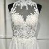 Cette robe de mariée allie raffinement et modernité avec son corsage en dentelle florale et son col haut élégant. Sa jupe fluide crée une silhouette aérienne, sublimée par un décor contemporain. Parfaite pour une mariée en quête de romantisme et de minimalisme.
