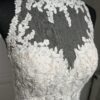 Cette robe de mariée allie raffinement et modernité avec son corsage en dentelle florale et son col haut élégant. Sa jupe fluide crée une silhouette aérienne, sublimée par un décor contemporain. Parfaite pour une mariée en quête de romantisme et de minimalisme.