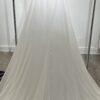 Cette robe de mariée allie raffinement et modernité avec son corsage en dentelle florale et son col haut élégant. Sa jupe fluide crée une silhouette aérienne, sublimée par un décor contemporain. Parfaite pour une mariée en quête de romantisme et de minimalisme.
