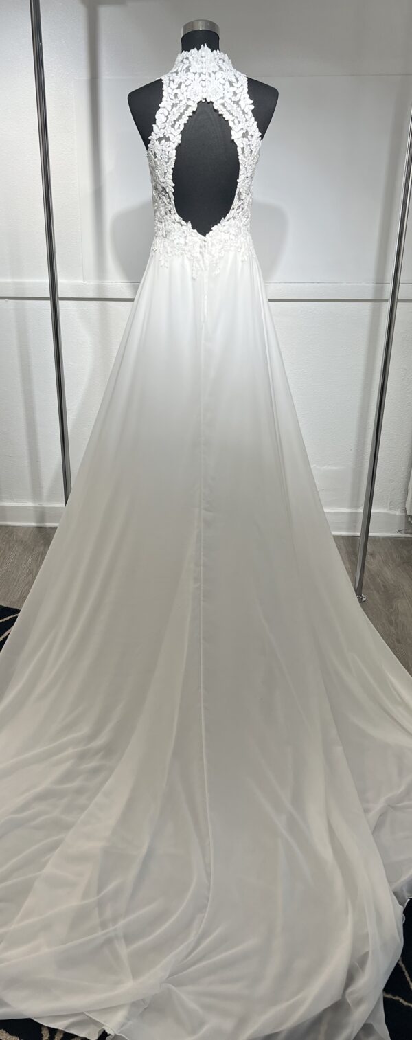 Cette robe de mariée allie raffinement et modernité avec son corsage en dentelle florale et son col haut élégant. Sa jupe fluide crée une silhouette aérienne, sublimée par un décor contemporain. Parfaite pour une mariée en quête de romantisme et de minimalisme.