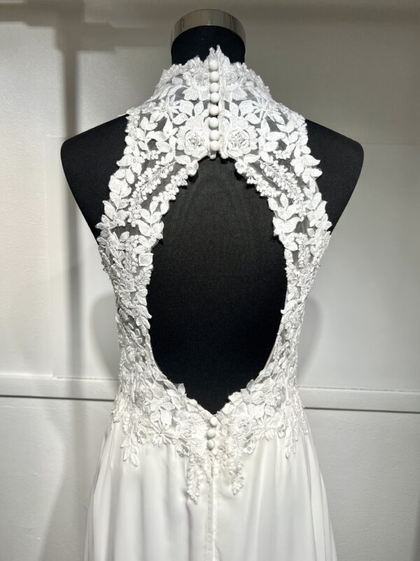 Cette robe de mariée allie raffinement et modernité avec son corsage en dentelle florale et son col haut élégant. Sa jupe fluide crée une silhouette aérienne, sublimée par un décor contemporain. Parfaite pour une mariée en quête de romantisme et de minimalisme.