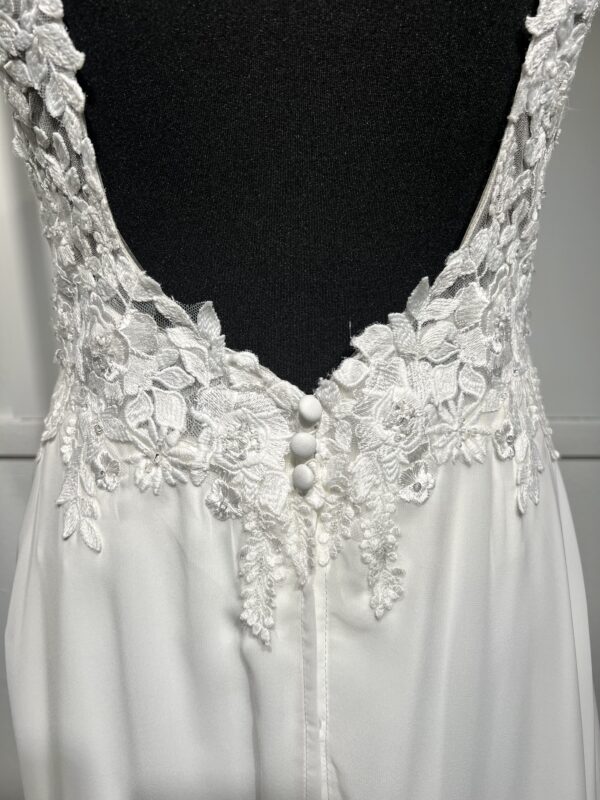 Cette robe de mariée allie raffinement et modernité avec son corsage en dentelle florale et son col haut élégant. Sa jupe fluide crée une silhouette aérienne, sublimée par un décor contemporain. Parfaite pour une mariée en quête de romantisme et de minimalisme.