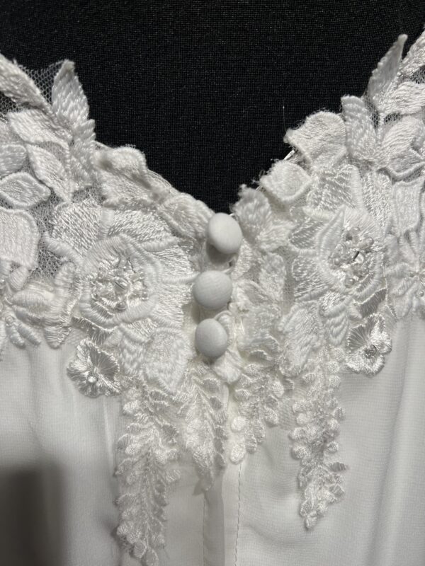 Cette robe de mariée allie raffinement et modernité avec son corsage en dentelle florale et son col haut élégant. Sa jupe fluide crée une silhouette aérienne, sublimée par un décor contemporain. Parfaite pour une mariée en quête de romantisme et de minimalisme.