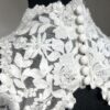 Cette robe de mariée allie raffinement et modernité avec son corsage en dentelle florale et son col haut élégant. Sa jupe fluide crée une silhouette aérienne, sublimée par un décor contemporain. Parfaite pour une mariée en quête de romantisme et de minimalisme.