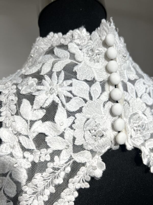 Cette robe de mariée allie raffinement et modernité avec son corsage en dentelle florale et son col haut élégant. Sa jupe fluide crée une silhouette aérienne, sublimée par un décor contemporain. Parfaite pour une mariée en quête de romantisme et de minimalisme.