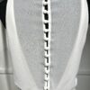 Une robe de mariée blanche minimaliste, avec un haut fluide sans manches et une jupe droite. Elle se distingue par sa simplicité élégante, mise en valeur dans un couloir moderne en pierre.