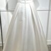Une robe de mariée princesse avec un col carré structuré et une jupe ample, posant dans une allée bordée d’un château majestueux.