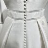 Une robe de mariée princesse avec un col carré structuré et une jupe ample, posant dans une allée bordée d’un château majestueux.