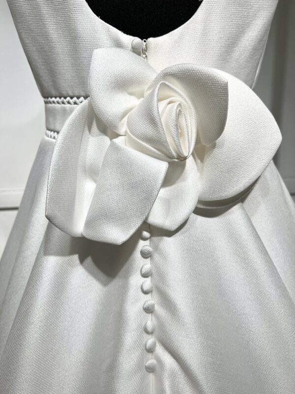 Une robe de mariée princesse à col carré et jupe volumineuse, devant un paysage moderne baigné de lumière.