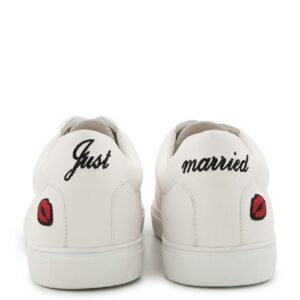 Vue arrière d’une paire de baskets blanches avec les inscriptions « Just » et « married » en noir et des broderies rouges de lèvres.