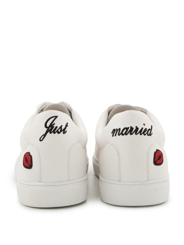 Vue arrière d’une paire de baskets blanches avec les inscriptions « Just » et « married » en noir et des broderies rouges de lèvres.