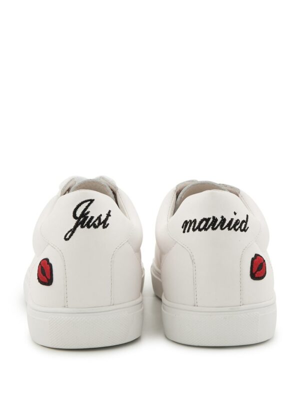 Vue arrière d’une paire de baskets blanches avec les inscriptions « Just » et « married » en noir et des broderies rouges de lèvres.