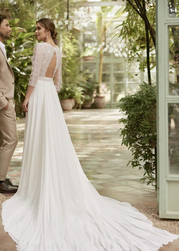 Vue de dos d'une robe de mariée en dentelle avec une longue traîne fluide dans un jardin intérieur