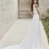 Vue arrière d'une robe de mariée avec un haut fluide et une longue traîne élégante s’étalant dans un couloir moderne en pierre.