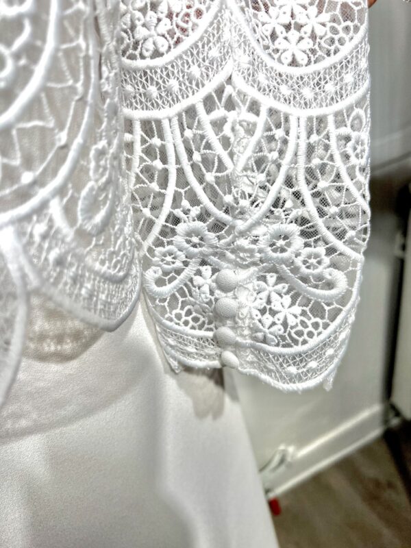 Mariée en robe de mariée en dentelle avec manches trois-quarts, posant dans un cadre floral intérieur