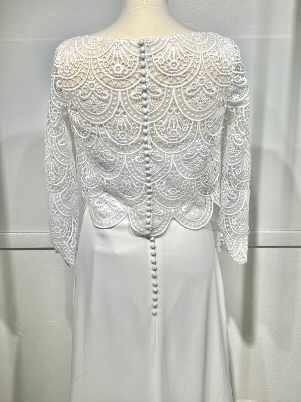 Mariée en robe de mariée en dentelle avec manches trois-quarts, posant dans un cadre floral intérieur