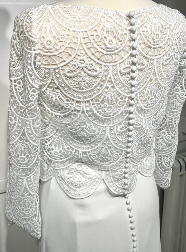 Mariée en robe de mariée en dentelle avec manches trois-quarts, posant dans un cadre floral intérieur