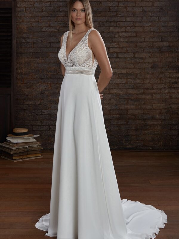 Une robe de mariée fluide avec un corsage en dentelle délicate à motifs géométriques, des bretelles épaisses et une jupe lisse évasée tombant gracieusement jusqu’au sol