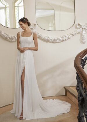 Cette robe de mariée allie romantisme et modernité avec son corsage en dentelle délicate et sa jupe fluide à fente élégante. Sa traîne légère et son cadre raffiné subliment une allure chic et intemporelle.