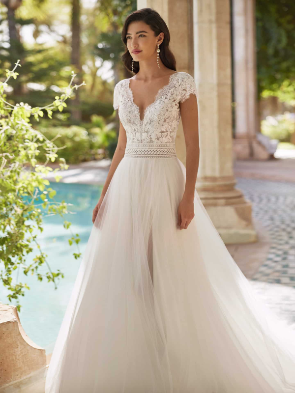 Mariée en robe de mariée avec corsage en dentelle et fente latérale, posant devant des colonnes en pierre