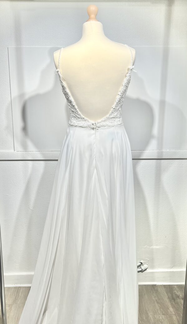 Robe de mariée à bretelles fines avec décolleté en V profond, ornée de dentelle florale délicate, portée par une femme élégante devant un mur en pierre naturel