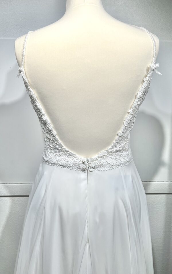Robe de mariée à bretelles fines avec décolleté en V profond, ornée de dentelle florale délicate, portée par une femme élégante devant un mur en pierre naturel