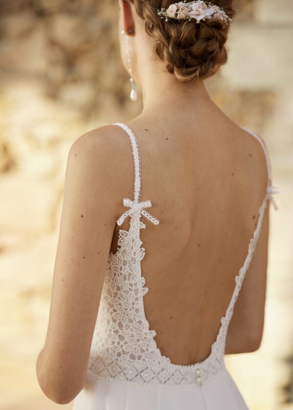 Gros plan de la partie supérieure d'une robe de mariée en dentelle avec un dos échancré et des bretelles fines ornées de nœuds