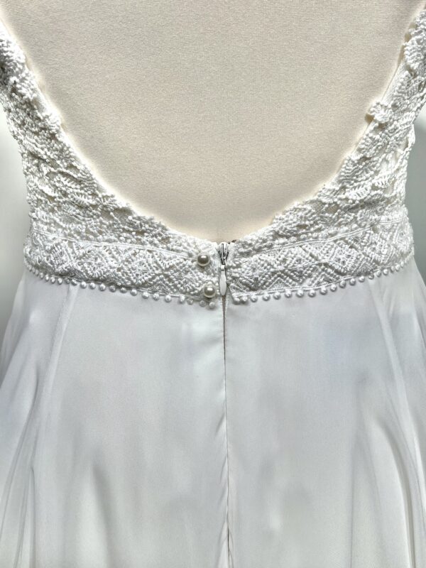 Robe de mariée à bretelles fines avec décolleté en V profond, ornée de dentelle florale délicate, portée par une femme élégante devant un mur en pierre naturel