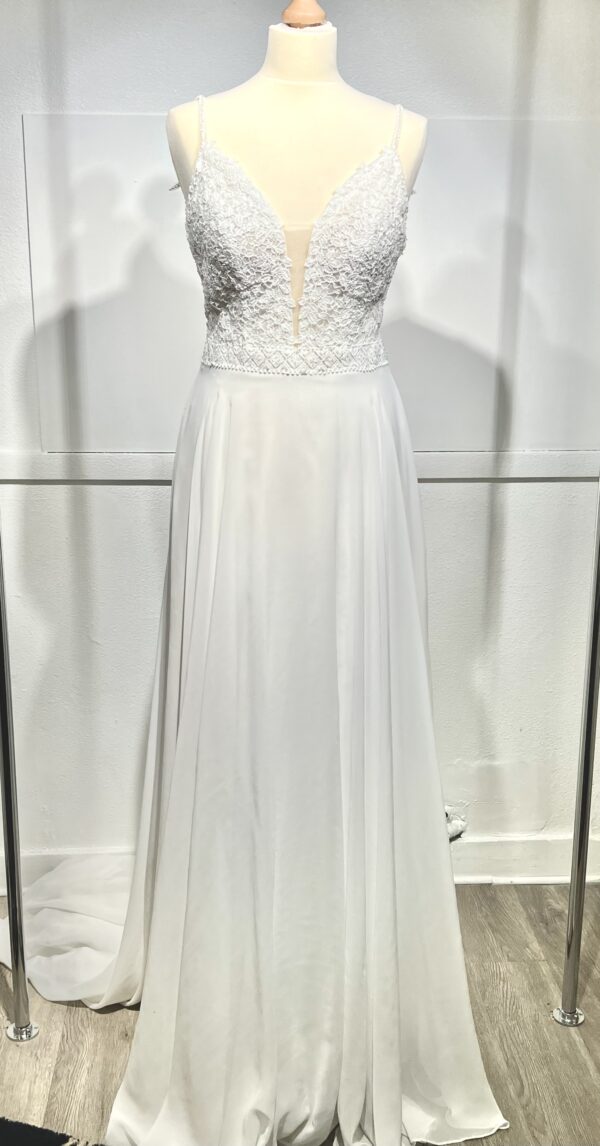Robe de mariée à bretelles fines avec décolleté en V profond, ornée de dentelle florale délicate, portée par une femme élégante devant un mur en pierre naturel