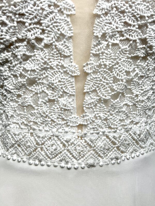 Robe de mariée à bretelles fines avec décolleté en V profond, ornée de dentelle florale délicate, portée par une femme élégante devant un mur en pierre naturel