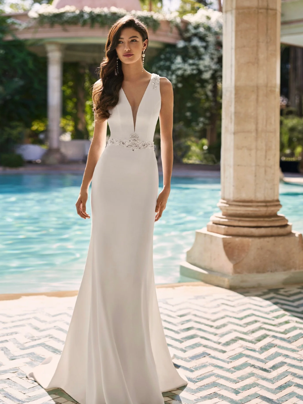 Mariée élégante portant une robe de mariée ajustée avec un décolleté en V profond et des détails scintillants à la taille, posant devant une piscine
