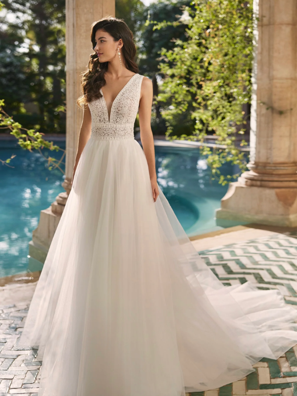 Mariée posant élégamment en robe de mariée avec un décolleté en V profond près d'une piscine, dans un cadre romantique en extérieur