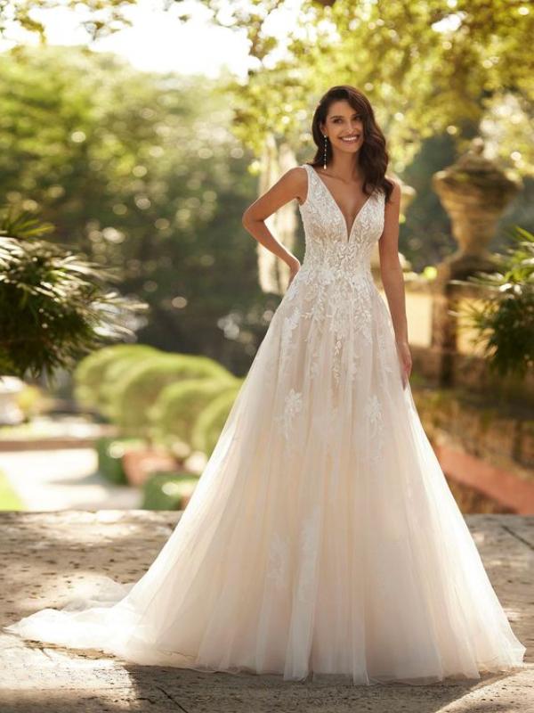 Mariée portant une robe de mariée en tulle avec un décolleté en cœur, broderies florales et bretelles fines, posant dans un jardin ensoleillé