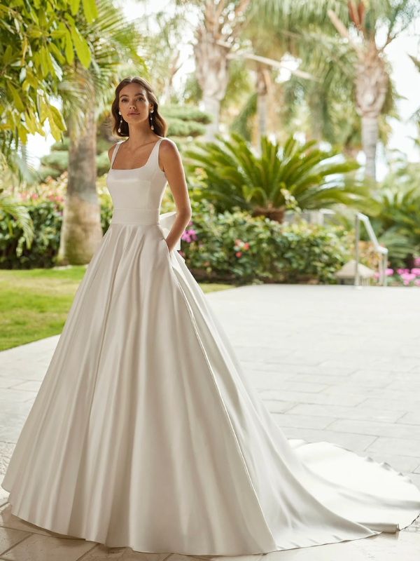 Mariée élégante portant une robe de mariée Mikado satinée avec un col carré et une jupe volumineuse, posant dans un cadre tropical