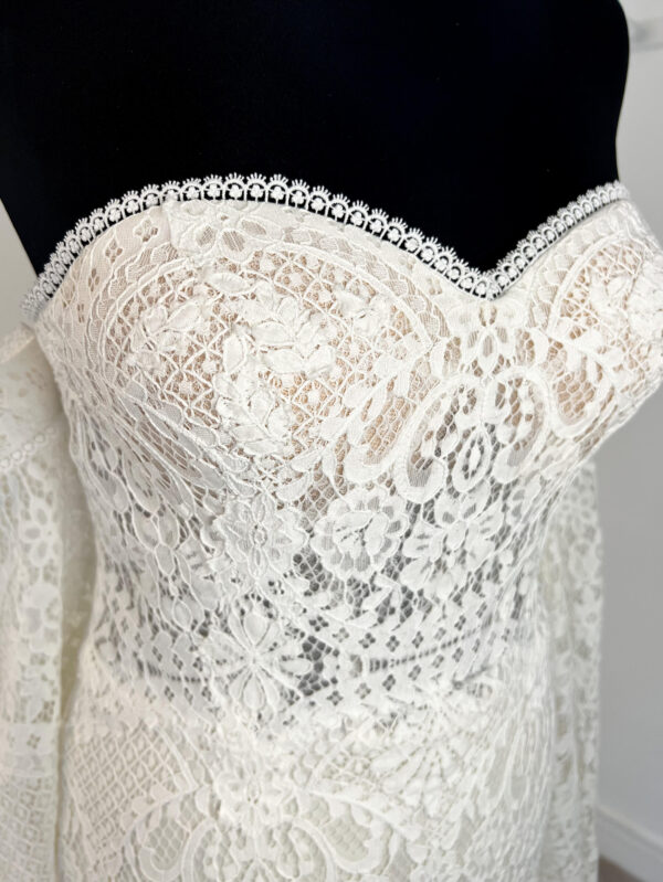 Robe de mariée en dentelle à manches trois-quarts avec détails floraux, avec une mariée élégante en pleine conversation avec un homme en costume beige