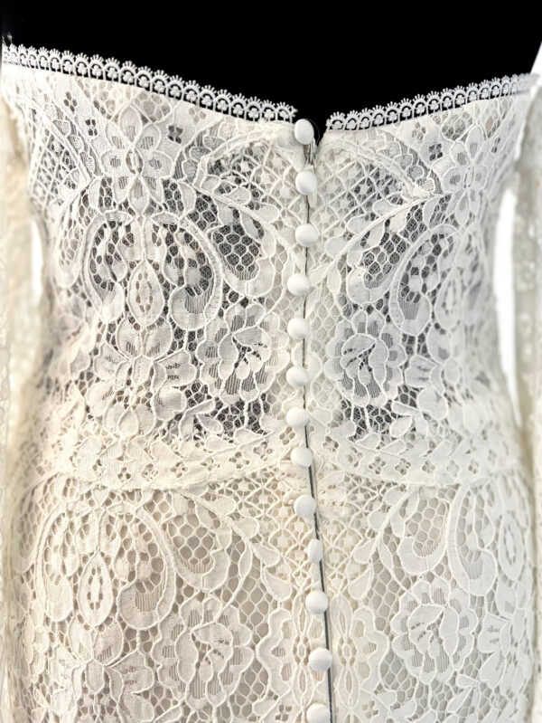 Robe de mariée en dentelle à manches trois-quarts avec détails floraux, avec une mariée élégante en pleine conversation avec un homme en costume beige
