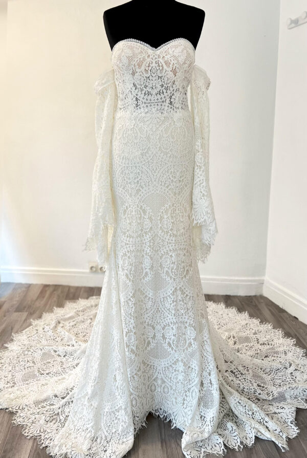 Robe de mariée en dentelle à manches trois-quarts avec détails floraux, avec une mariée élégante en pleine conversation avec un homme en costume beige