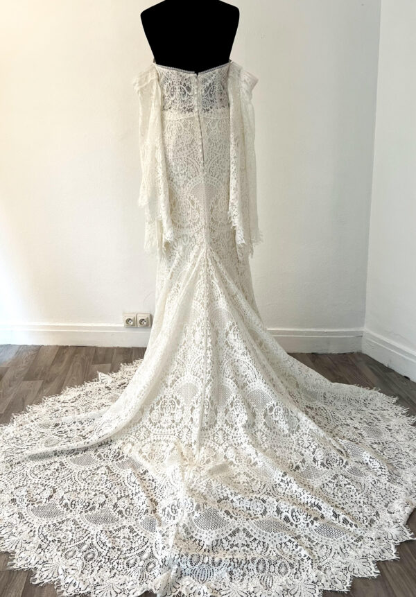 Robe de mariée en dentelle à manches trois-quarts avec détails floraux, avec une mariée élégante en pleine conversation avec un homme en costume beige